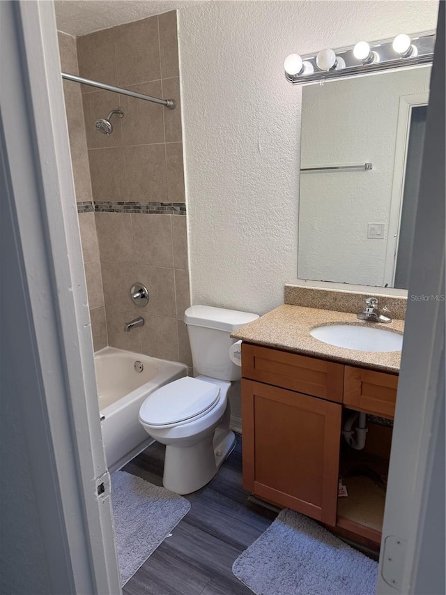 bathroom featuring a textured wall, toilet, wood finished floors, vanity, and washtub / shower combination