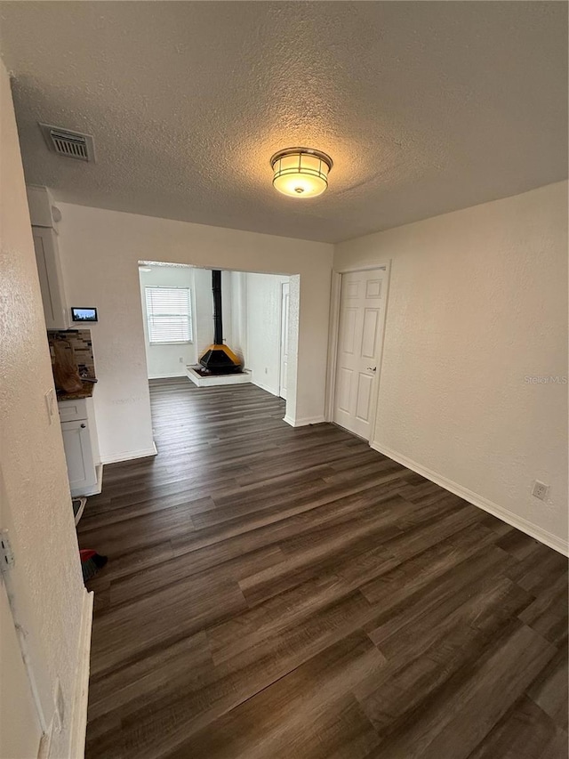 unfurnished dining area with a textured ceiling, visible vents, baseboards, dark wood finished floors, and a wood stove