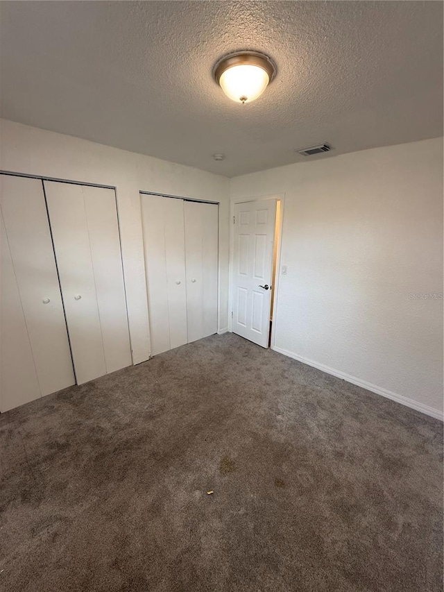 unfurnished bedroom with carpet floors, a textured ceiling, visible vents, and multiple closets