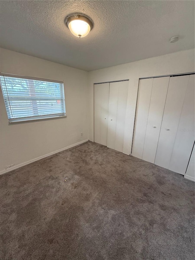 unfurnished bedroom featuring a textured ceiling, carpet flooring, and multiple closets