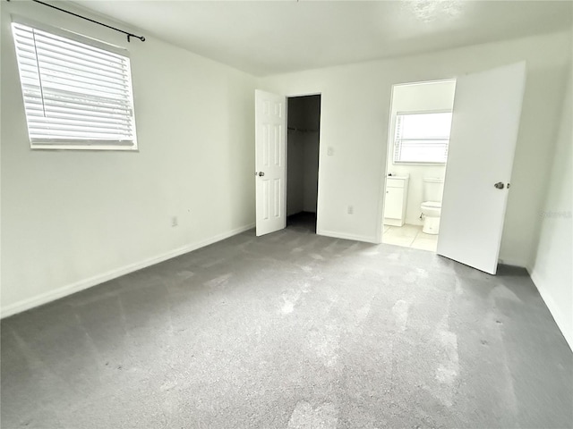 unfurnished bedroom with a spacious closet, a closet, ensuite bath, and baseboards