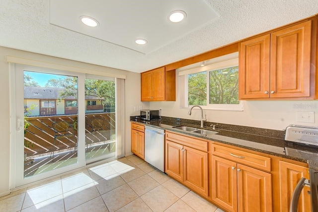 kitchen with sink, dark stone countertops, light tile patterned floors, stainless steel appliances, and a textured ceiling