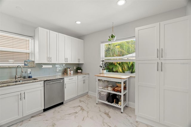 kitchen featuring light stone countertops, backsplash, stainless steel dishwasher, sink, and white cabinetry