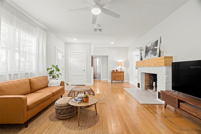 living room with ceiling fan, light wood-type flooring, and a brick fireplace