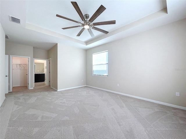 spare room with light colored carpet, a raised ceiling, and ceiling fan