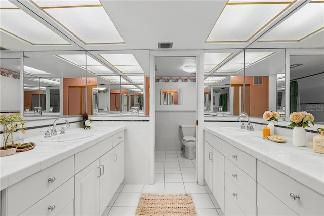 bathroom featuring tile patterned flooring, vanity, toilet, and tile walls