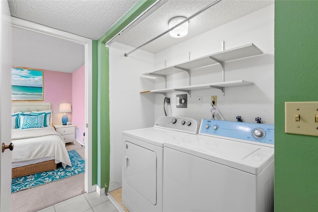 clothes washing area with washing machine and dryer, light tile patterned floors, and a textured ceiling