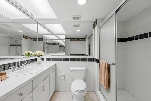 bathroom with vanity, tile patterned floors, toilet, tile walls, and a shower with shower door