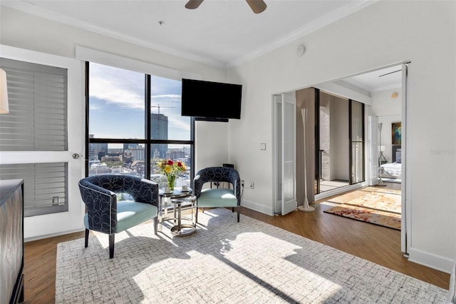 living area with baseboards, a ceiling fan, wood finished floors, and crown molding