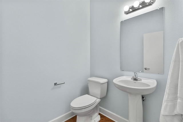 half bathroom with baseboards, toilet, and wood finished floors