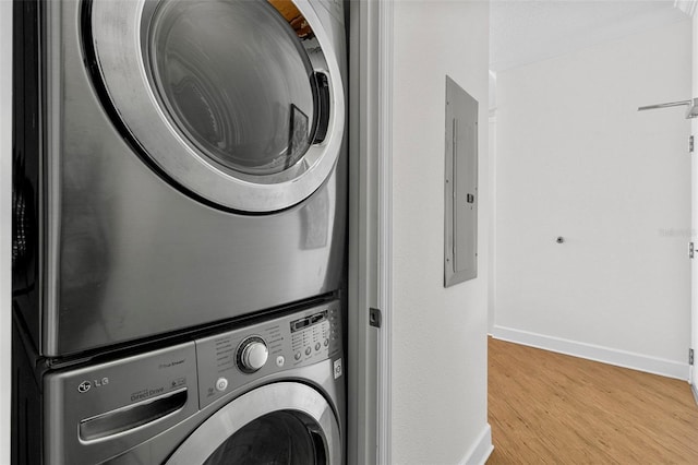 washroom featuring stacked washer and dryer, electric panel, wood finished floors, and baseboards