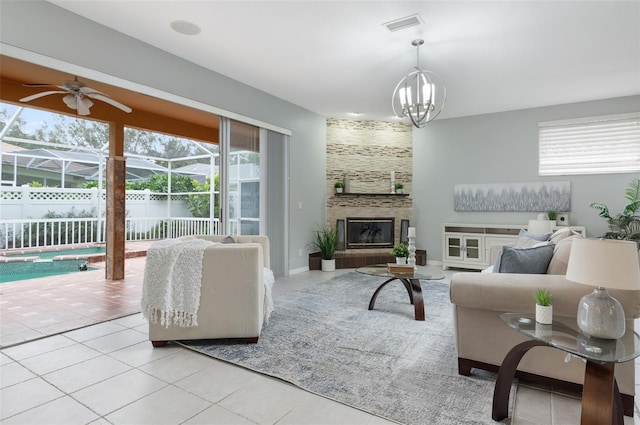 tiled living room with a large fireplace, a wealth of natural light, and ceiling fan with notable chandelier