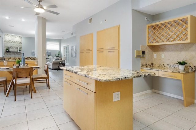 kitchen featuring ceiling fan, a center island, light stone countertops, light brown cabinets, and light tile patterned floors