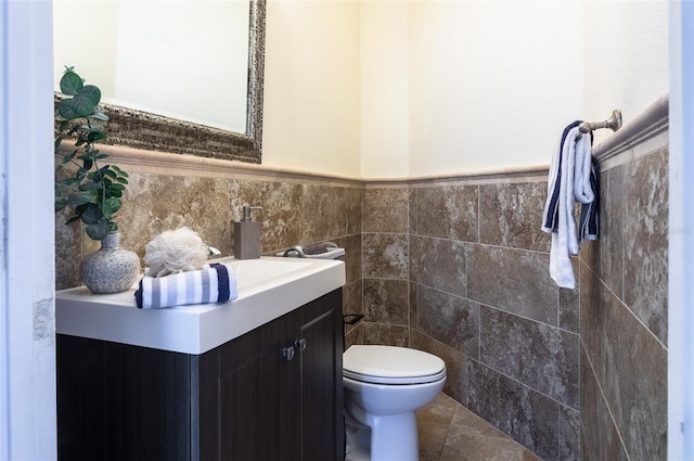 bathroom with toilet, tile patterned flooring, tile walls, and vanity