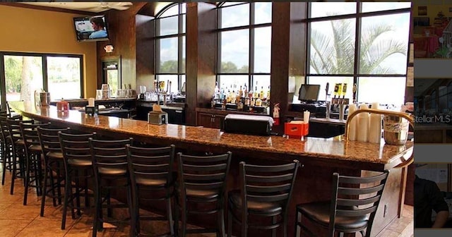 bar with stone counters, light tile patterned floors, and a wealth of natural light