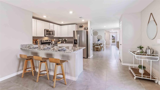 kitchen with kitchen peninsula, appliances with stainless steel finishes, light stone countertops, a kitchen breakfast bar, and white cabinetry