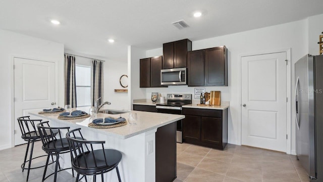 kitchen with a kitchen breakfast bar, dark brown cabinets, stainless steel appliances, sink, and a center island with sink