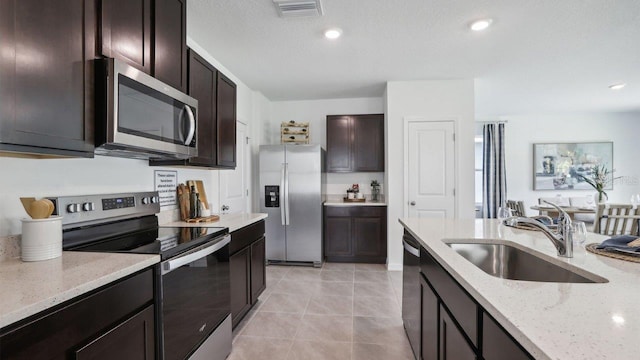 kitchen with dark brown cabinets, sink, light stone countertops, and stainless steel appliances