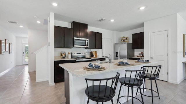 kitchen with dark brown cabinetry, sink, stainless steel appliances, a center island with sink, and light tile patterned flooring