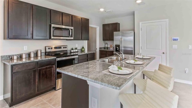 kitchen featuring sink, a kitchen island with sink, a breakfast bar, light tile patterned floors, and appliances with stainless steel finishes