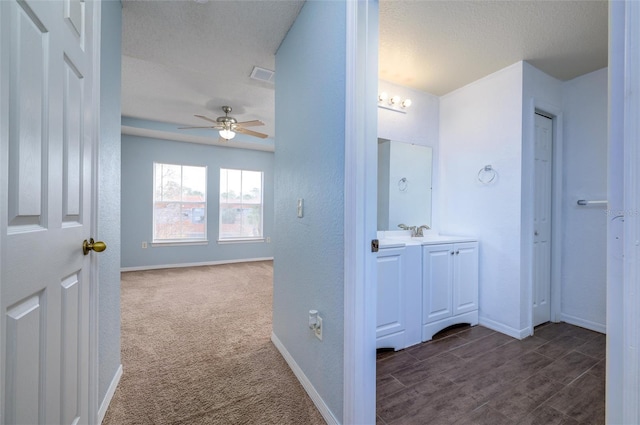 corridor featuring a textured ceiling, dark carpet, and sink