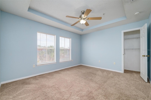 unfurnished bedroom featuring a textured ceiling, ceiling fan, light carpet, and a tray ceiling