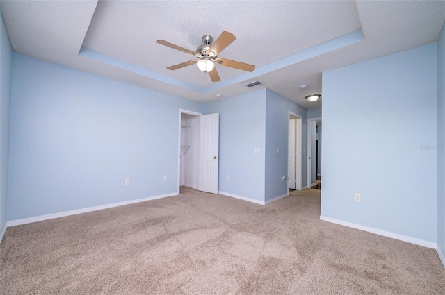 spare room featuring a textured ceiling, a tray ceiling, ceiling fan, and light colored carpet