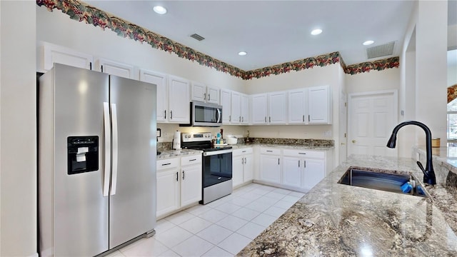 kitchen with sink, light tile patterned floors, light stone countertops, appliances with stainless steel finishes, and white cabinetry