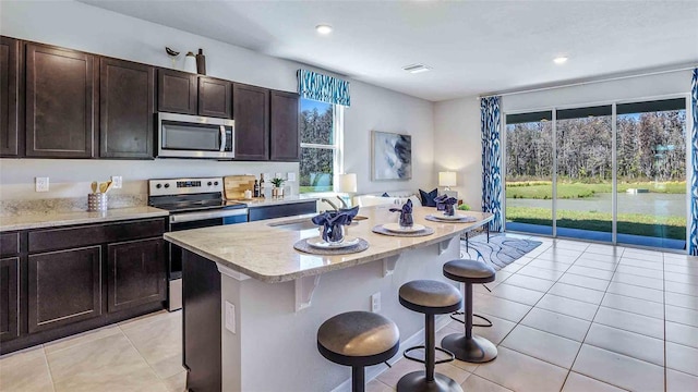 kitchen with a kitchen bar, appliances with stainless steel finishes, sink, light tile patterned floors, and an island with sink