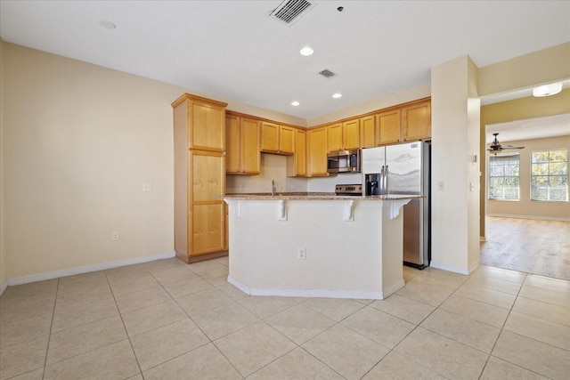 kitchen featuring a kitchen bar, light stone countertops, stainless steel appliances, ceiling fan, and a center island