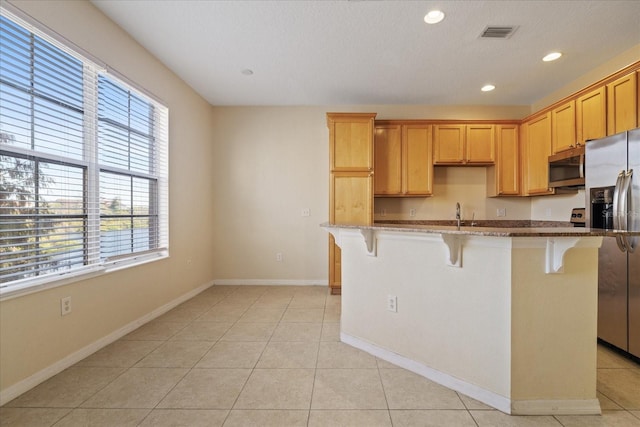 kitchen with a kitchen bar, light stone counters, stainless steel appliances, a center island with sink, and light tile patterned flooring