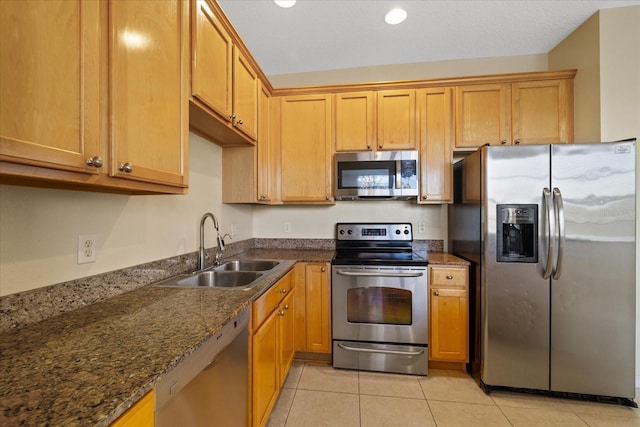 kitchen featuring dark stone countertops, sink, light tile patterned floors, and appliances with stainless steel finishes