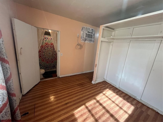 unfurnished bedroom with ensuite bathroom, hardwood / wood-style floors, a wall unit AC, and a closet