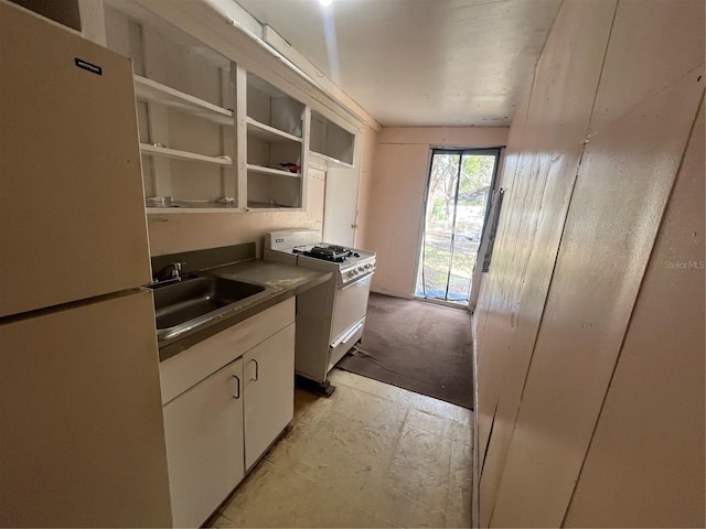 kitchen featuring sink, fridge, white cabinets, and white gas range