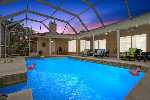 pool at dusk with a lanai, a patio area, and ceiling fan