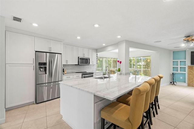 kitchen with a kitchen island with sink, sink, appliances with stainless steel finishes, light stone counters, and white cabinetry