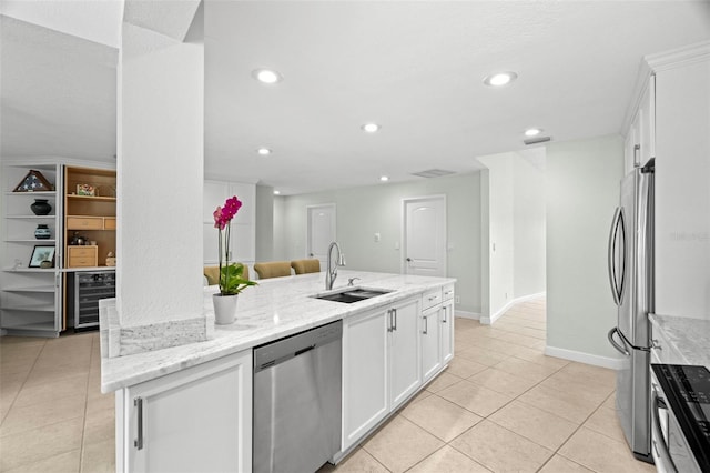 kitchen with appliances with stainless steel finishes, light stone counters, sink, a center island with sink, and white cabinetry