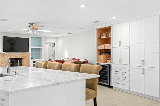 kitchen featuring beverage cooler, light tile patterned floors, a kitchen breakfast bar, light stone counters, and white cabinets