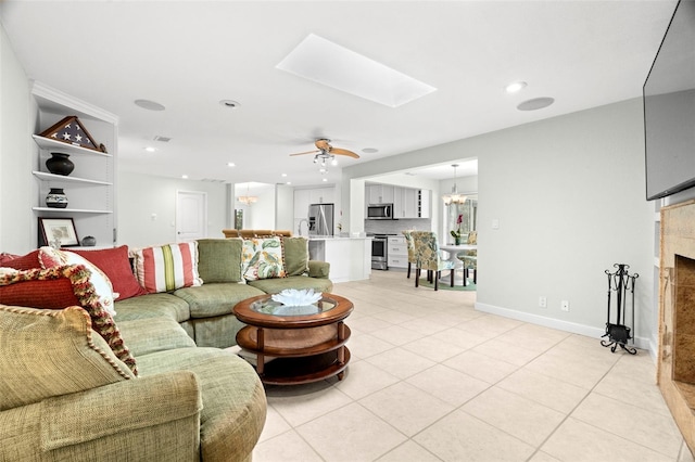 tiled living room featuring a skylight, a fireplace, and ceiling fan with notable chandelier