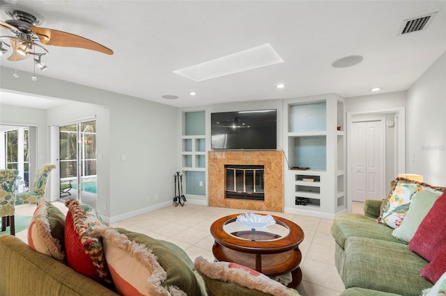 living room with built in shelves, ceiling fan, light tile patterned floors, and a skylight