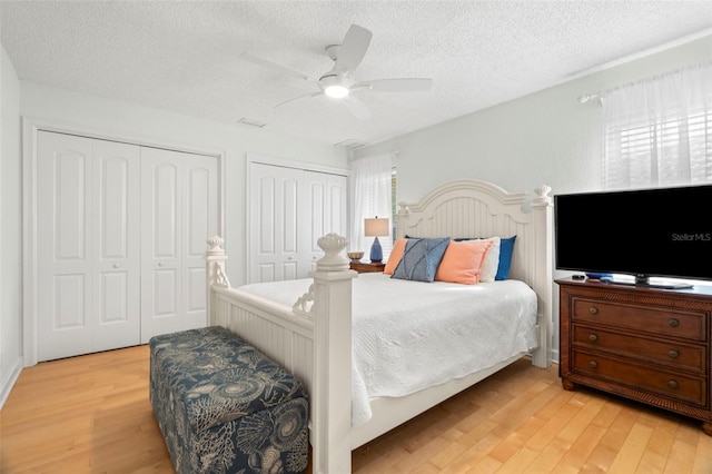 bedroom with a textured ceiling, two closets, ceiling fan, and light hardwood / wood-style floors