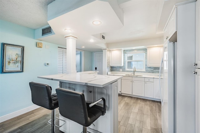 kitchen with ornate columns, white cabinetry, sink, decorative backsplash, and a breakfast bar