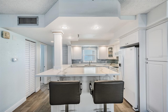 kitchen with sink, white refrigerator with ice dispenser, white cabinets, hardwood / wood-style floors, and a breakfast bar area