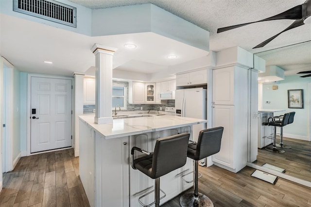 kitchen with decorative columns, white cabinetry, a kitchen bar, and wood-type flooring