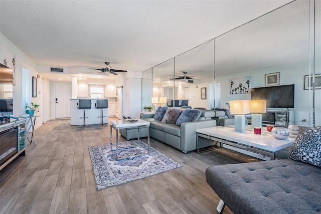 living room with a textured ceiling, light wood-type flooring, and ceiling fan