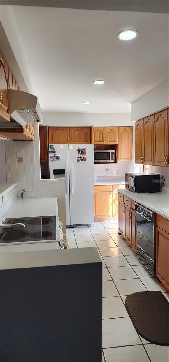 kitchen featuring exhaust hood, decorative backsplash, light tile patterned flooring, and black appliances