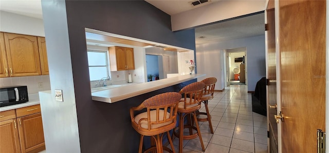 kitchen featuring sink, decorative backsplash, light tile patterned floors, kitchen peninsula, and a breakfast bar area