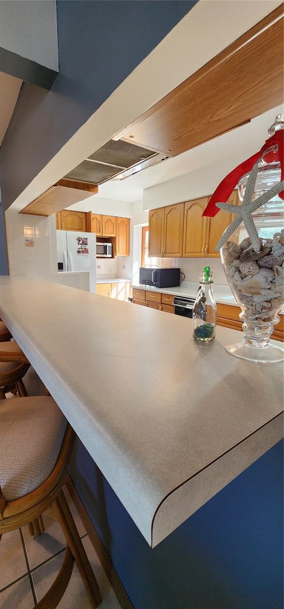 kitchen featuring light brown cabinets, tile patterned floors, a breakfast bar area, and black appliances