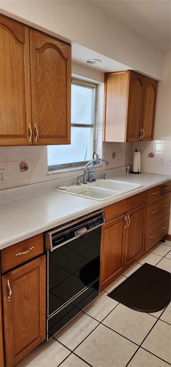 kitchen featuring decorative backsplash, sink, light tile patterned floors, and black dishwasher