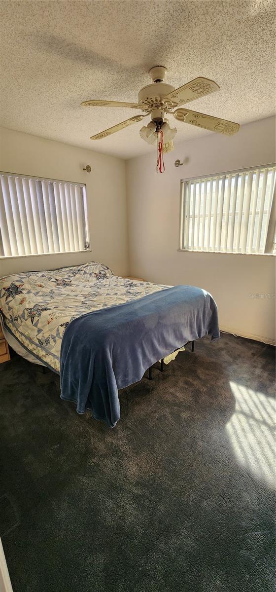 carpeted bedroom with ceiling fan and a textured ceiling